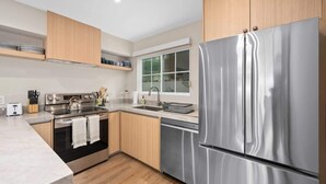 Une cuisine moderne dotée d’appareils électroménagers en acier inoxydable, de meubles en bois et d’une fenêtre laissant entrer la lumière naturelle.