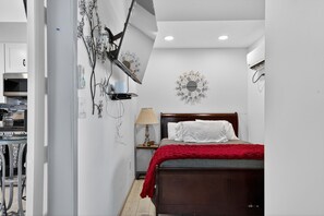 Een slaapkamer met een bed, een wandlamp, een decoratieve wandklok en een airconditioning.