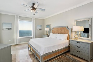 A bedroom with a bed, nightstands, a dresser, a ceiling fan, and a large window with a view.