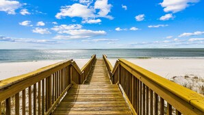 A wooden boardwalk leading to a beach with a clear sky and ocean in the background.