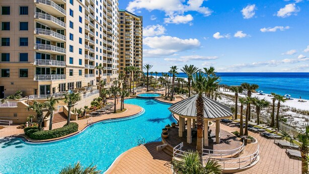 A resort with a large swimming pool, a beach area, and a view of the ocean.