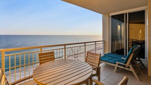 A balcony with a wooden table and chairs, a lounge chair, and a view of the ocean.