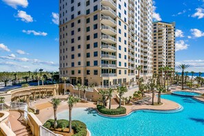 A high-rise hotel with multiple balconies, a swimming pool, and palm trees.