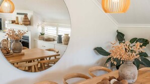 A dining area with a wooden table, chairs, and a mirror reflecting the room. There are vases with dried plants and a potted plant on the table. - Sabera - Penthouse in the heart of Byron Bay (Byron Bay)