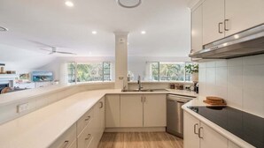 A modern kitchen with white cabinetry, a black countertop, and a window providing a view of greenery outside. - Sabera - Penthouse in the heart of Byron Bay (Byron Bay)