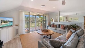A spacious living room with a large TV, a round coffee table, and a sofa. There is a sliding glass door leading to an outdoor area with a view of the ocean. - Sabera - Penthouse in the heart of Byron Bay (Byron Bay)