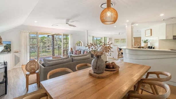 A modern kitchen with a central island, large windows, and a dining area with a wooden table and chairs. - Sabera - Penthouse in the heart of Byron Bay (Byron Bay)