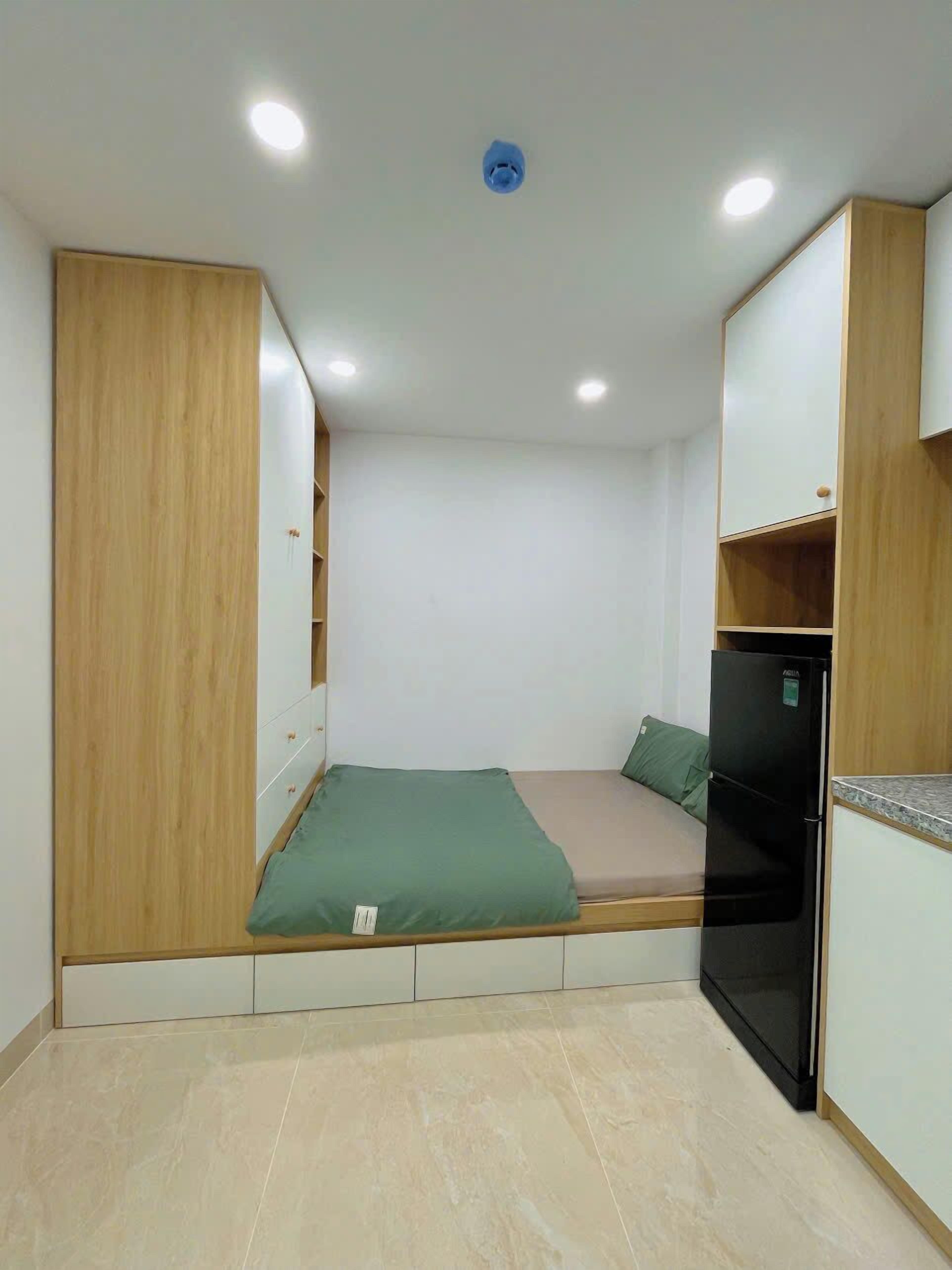 Una habitación compacta con cama, armario empotrado, kitchenette pequeña y una lámpara en el techo.