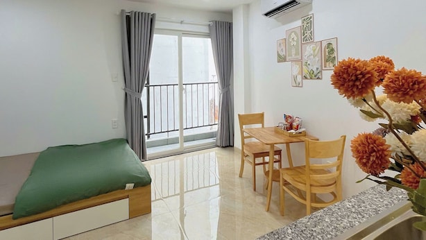 A modern living room with a sofa, a dining table with chairs, a kitchen area with a granite countertop and sink, and a balcony with curtains. - Hat Nang House - Go Vap (Ho Chi Minh City)