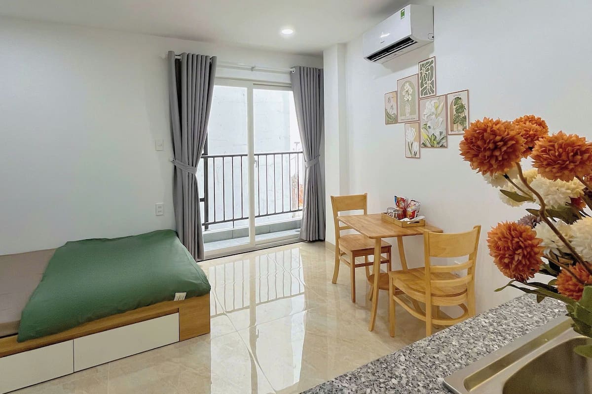 A modern living room with a sofa, a dining table with chairs, a kitchen area with a granite countertop and sink, and a balcony with curtains.