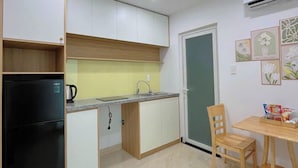 A compact kitchen with a black refrigerator, a sink, and a dining area with a wooden table and chairs. - Hat Nang House - Go Vap (Ho Chi Minh City)