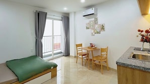 A compact living space with a bed, a small dining table with chairs, a kitchenette with a sink, and a window with curtains. - Hat Nang House - Go Vap (Ho Chi Minh City)