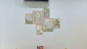 A room with a white air conditioner, a wooden table with two chairs, and six framed artworks on the wall. - Hat Nang House - Go Vap (Ho Chi Minh City)