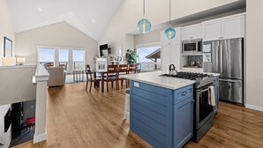 A modern kitchen with a central island, stainless steel appliances, and a dining area with a view. - Eagle's View - Luxury townhome. Amazing views. (Pacific City)