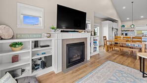 A modern living room with a fireplace, TV, and dining area. - Eagle's View - Luxury townhome. Amazing views. (Pacific City)