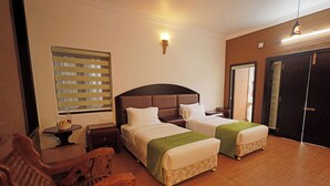 Habitación de hotel con dos camas, muebles de madera, un aplique en la pared y una ventana con persianas.