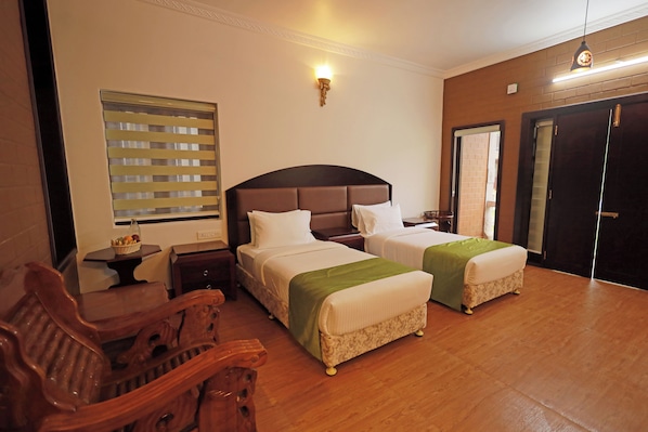 Une chambre d’hôtel avec deux lits, des meubles en bois, un luminaire fixé au mur et une fenêtre avec des stores.