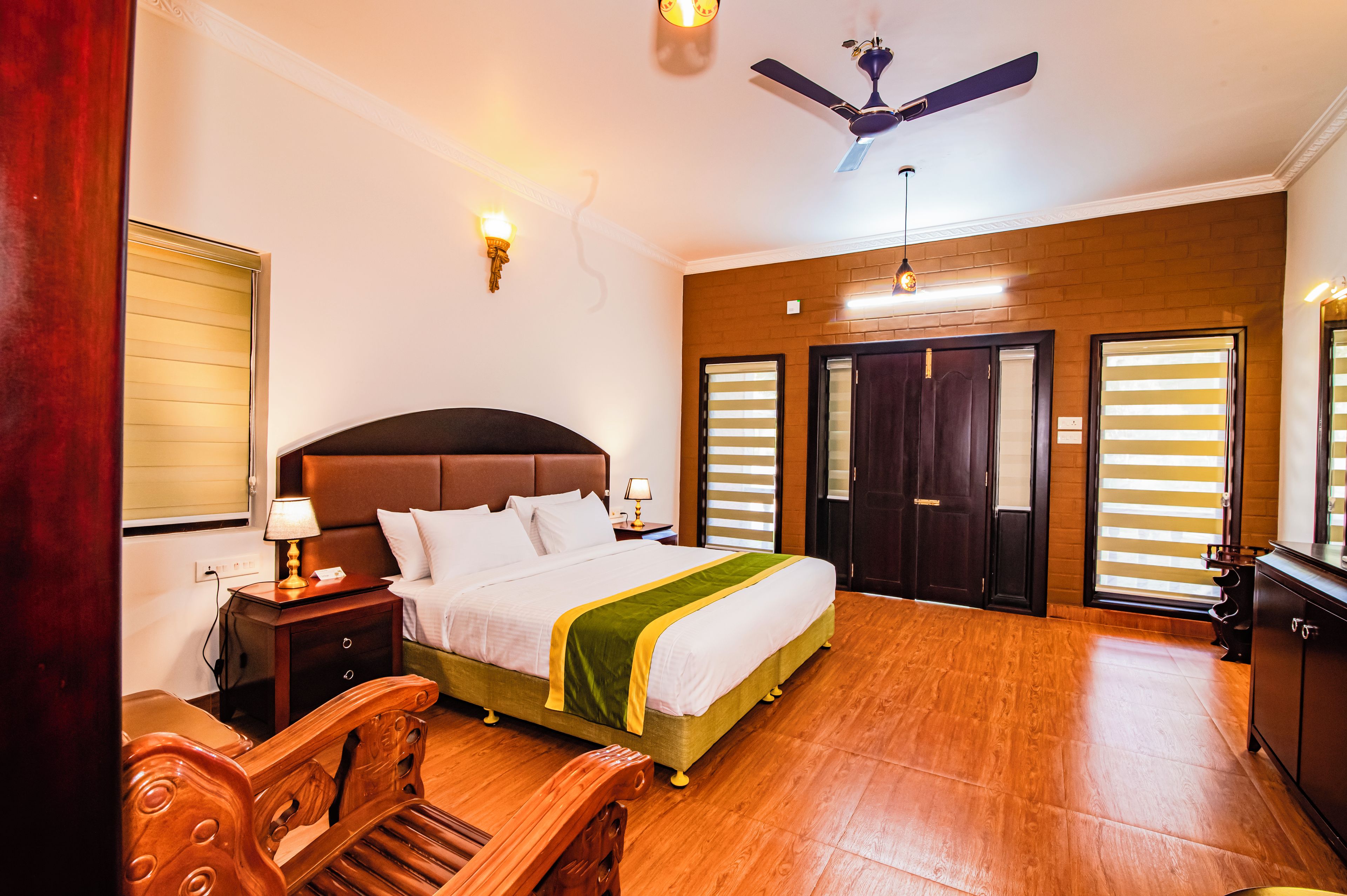 A hotel room with a bed, bedside tables, a ceiling fan, and a view of the outside through the windows.