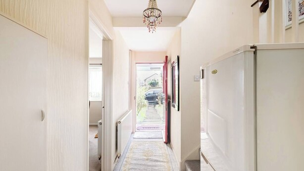 A narrow hallway with a carpet, a refrigerator, and a door leading to an outdoor area.