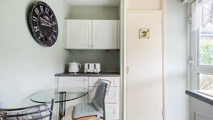 A compact kitchen with white cabinets, a kettle, a toaster, and a glass table with chairs.