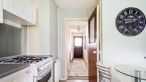 A narrow kitchen with a gas stove, oven, and a glass table with a towel.
