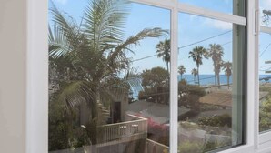 Blick durch ein Fenster mit weißem Rahmen, zeigt Palmen und eine Wohngegend mit Häusern unter blauem Himmel.