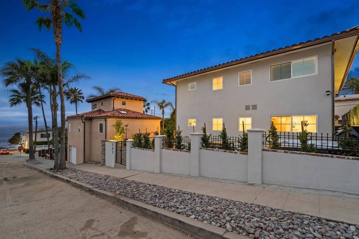 A two-story house with a white exterior, a tiled roof, and a gated driveway.