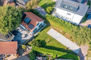 An aerial view of a residential area with a modern house featuring a sloped roof, a patio with outdoor furniture, and a well-maintained lawn. - Spacious 6-person Holiday Home Near De Koog (De Koog)
