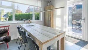 Ein moderner Essbereich mit einem Holztisch und Stühlen, großen Fenstern und Blick ins Freie.