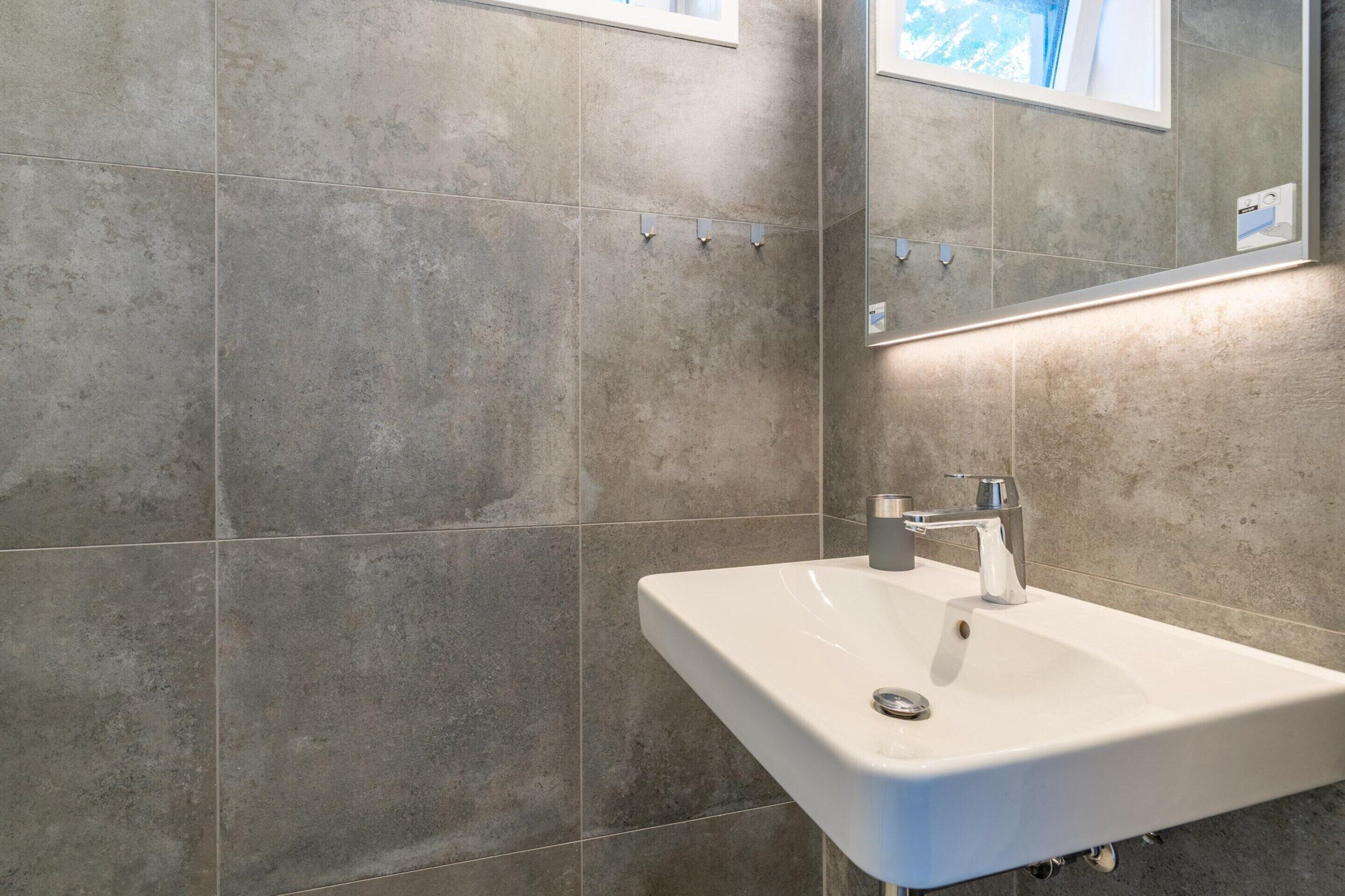 Ein Badezimmer mit weißem Waschbecken, einem Spiegel und gefliesten Wänden.