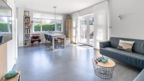 Ein modernes Wohnzimmer mit einer grauen Couch, einem Holztisch und einem Essbereich mit Tisch und Stühlen.