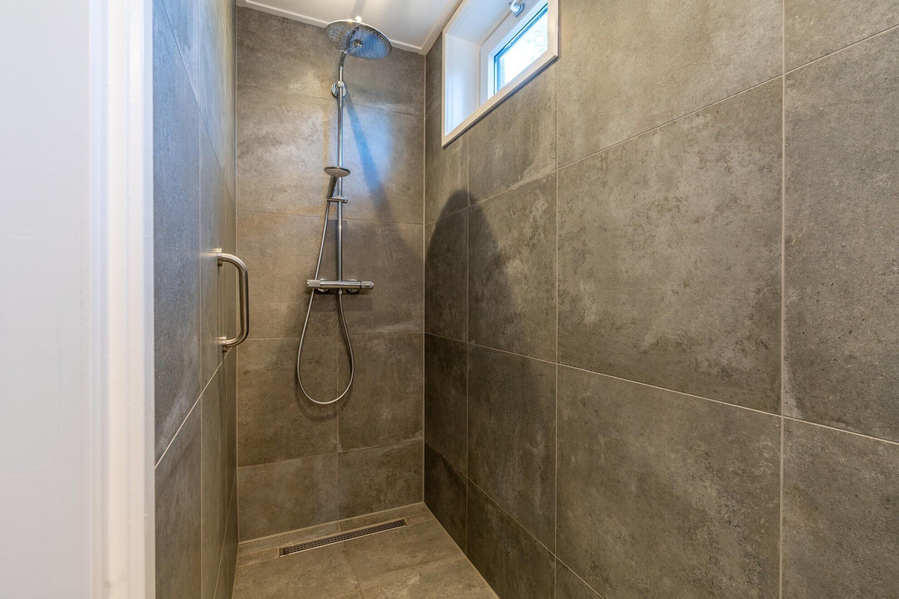 Un espacio de ducha pequeño y cerrado, con un cabezal de ducha de mano y un grifo en la pared.