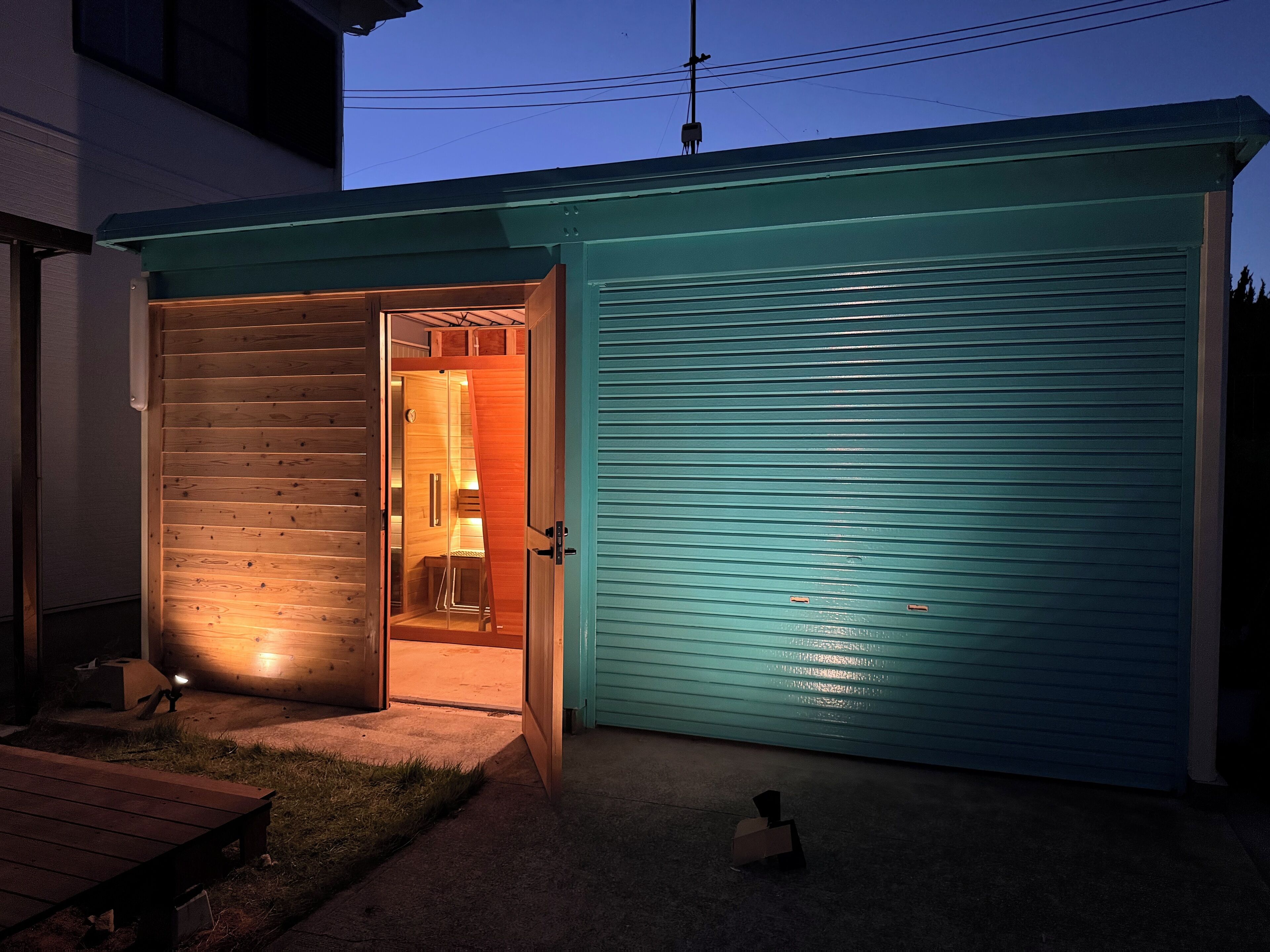 A garage with a wooden door and a blue shutter, a bench, and a small table outside.