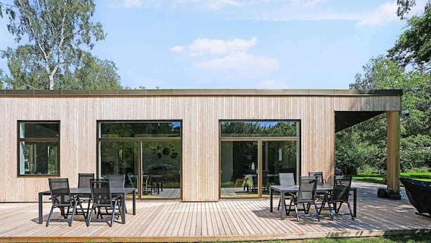 A modern house with a wooden exterior, large sliding glass doors, and a deck with outdoor furniture. - 5 Star Holiday Home in Frederiksvaerk (Frederiksvaerk)