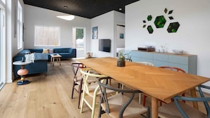 A modern living space with a wooden dining table, blue sofa, and a kitchen area with a TV and decorative wall art. - 5 Star Holiday Home in Frederiksvaerk (Frederiksvaerk)