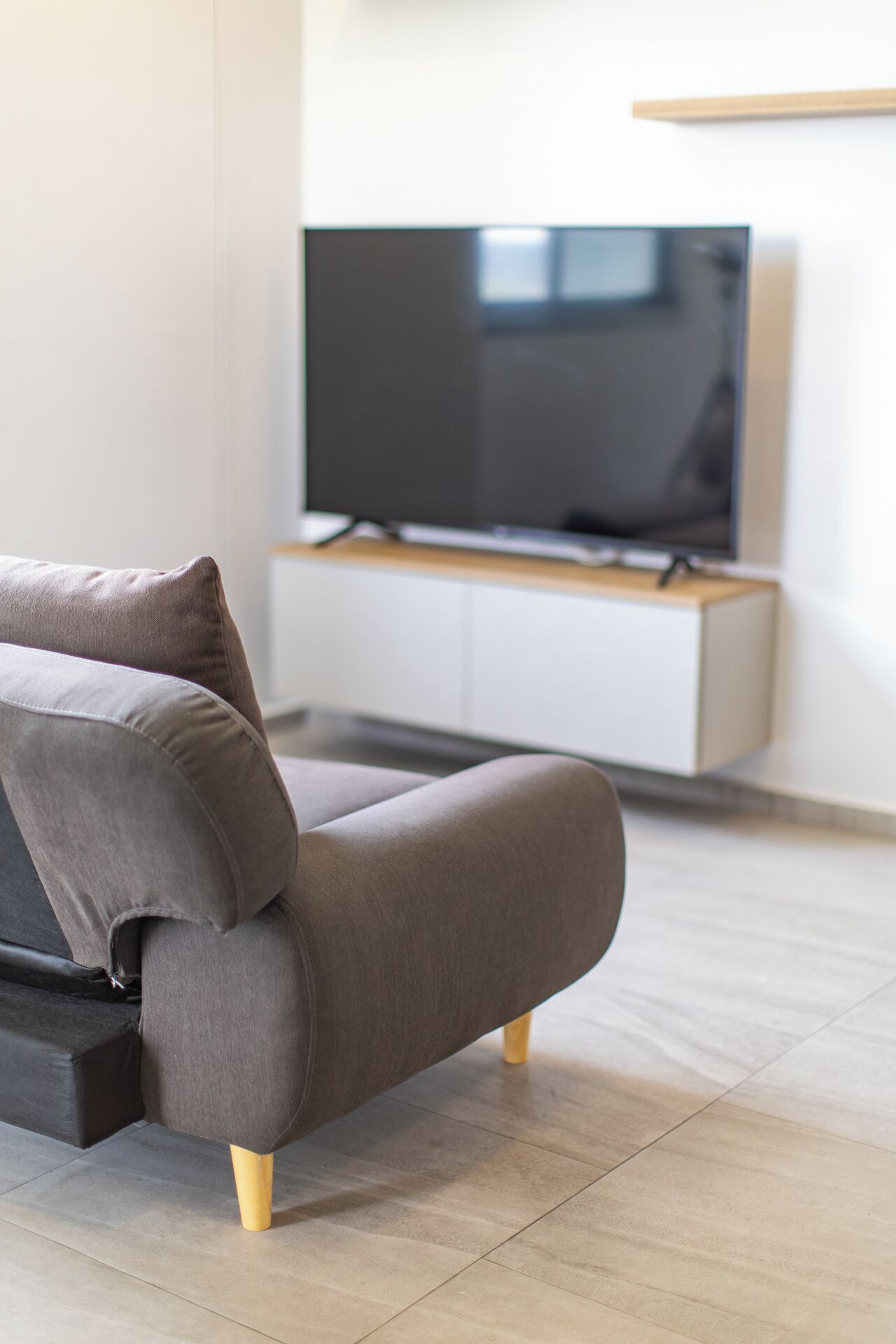 En moderne stue med en grå sofa, træben og et fladskærms-tv på et hvidt skab.