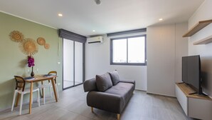 Una sala moderna con un sofá gris, una mesa de comedor con sillas, un televisor y un ventanal grande.