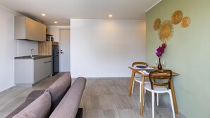 Una sala moderna con un sofá, una mesa de comedor con sillas y una cocina al fondo.
