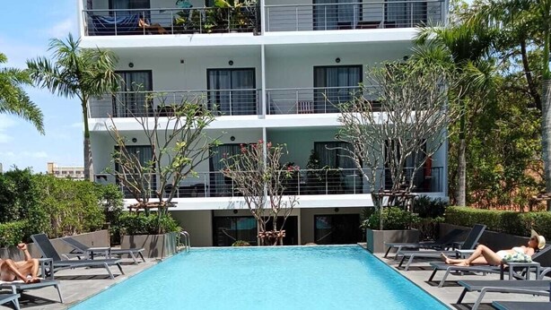 Un hotel de varios pisos con piscina, tumbonas y un jardín bien cuidado.