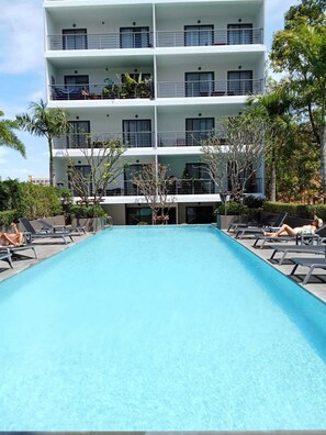 A multi-story hotel with a swimming pool, sun loungers, and a well-maintained garden. - Cozy Apt-1BR T3-635 (Chalong)