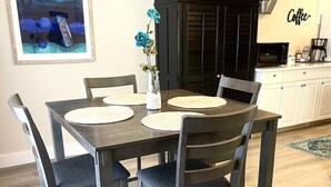 Ein Essbereich mit einem dunklen Holztisch und Stühlen, einer Vase mit blauen Blumen und einer Küche im Hintergrund.