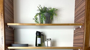 Eine Küche mit Holzregalen, einer Pflanze, einer Kaffeemaschine, Salz- und Pfefferstreuern, einem Spülbecken und Spülmittel.
