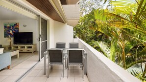 A balcony with a TV, seating, and lush greenery.