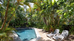 A swimming pool surrounded by lush tropical vegetation, with a paved patio and two lounge chairs. - Tea Trees 5 - Coastal Calm near Hastings St (Noosa Heads)
