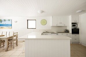 Une cuisine moderne avec des meubles blancs, un îlot central et un coin repas doté de chaises en bois.