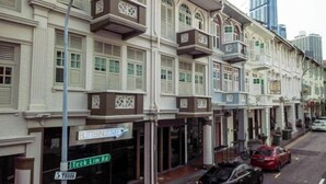 Une rangée de bâtiments traditionnels de style colonial, dotés de balcons, un panneau de signalisation indiquant la rue Teck Lim, et des voitures garées le long du trottoir.