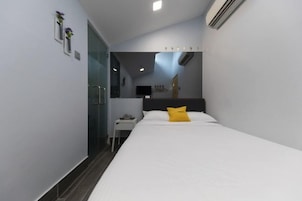 Una habitación de hotel moderna con una cama, una mesita de noche, un espejo y un pequeño escritorio con una silla.