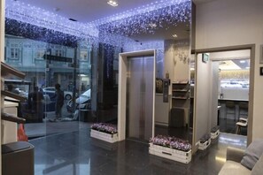 A modern lobby with a glass wall, an elevator, and a seating area with a coffee machine. - Butternut Tree Hotel (Singapore)