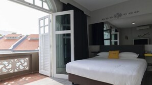 Une chambre d’hôtel avec un grand lit, une porte-fenêtre coulissante donnant sur un balcon et une vue sur le paysage urbain.