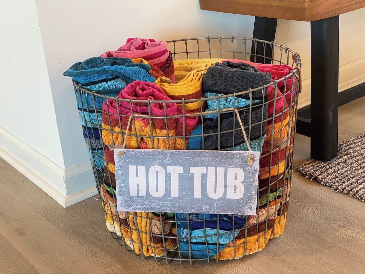 Ein Drahtkorb mit der Aufschrift „HOT TUB“, gefüllt mit bunten Handtüchern.